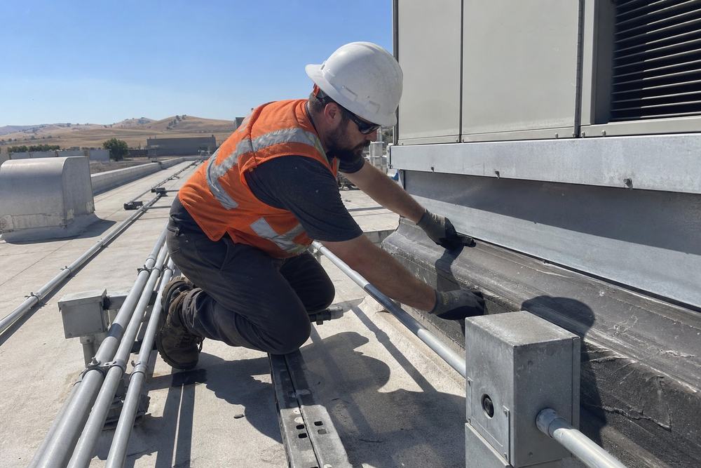 Roofing technician inspecting flashing around a rooftop mechanical unit curb